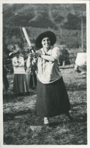A woman wearing a broad-brimmed hat poses with a bat over her right shoulder.