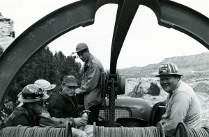 Five men sit in the back of a cable truck. In the background is a desert landscape.