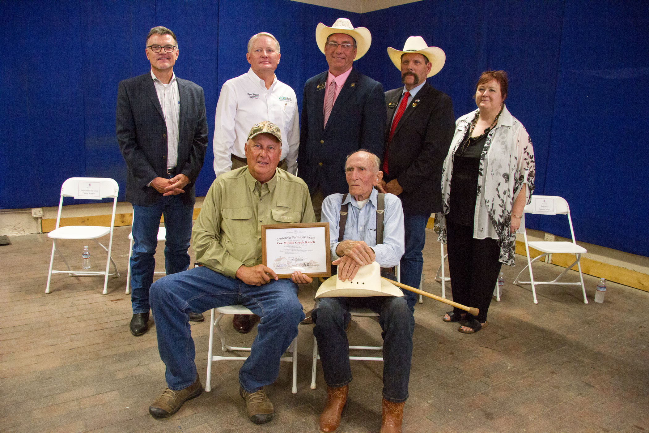 Members of the Coe Middle Creek Ranch sit holding their certificate.  State officials stand behind them.