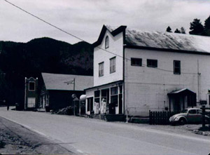 A black and white photo of the white building with sloping roof and road in front. 