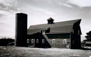 A photo of a barn and silo on the left in black and white. 