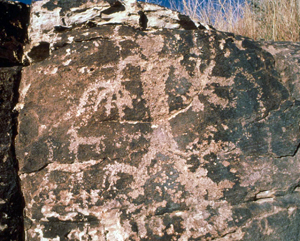 A picture of a rock with a carving of a person and some animals on it. 