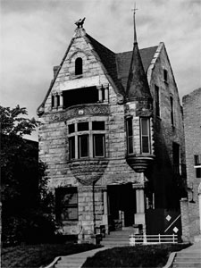 A black and white photo of the house with a corner turret and oriel window. There is a steep gabled roof and an entrance on the corner of the first floor. 