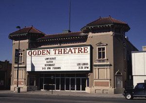 A view of the front of the theater from a slight angle. There are two cupolar roofs at either end and a prominent marquee with the name of the theater in the center over a large entry way.
