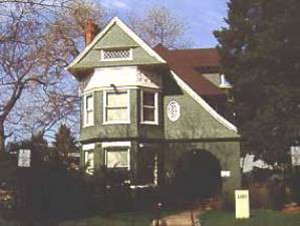 A photo of the house between a leafless tree on the left and evergreen on the right. 