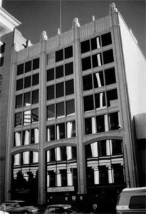 A black and white photo of the building from a very slight angle with rows and columns of windows and ornamented top. 
