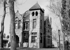 A black and white photo of the tall house with large leafless trees in the foreground and square corner tower in the center. 