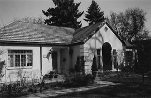 A black and white photo of the ranch style house with gabled roof and plain walls with arched entrance on the end of the house. 