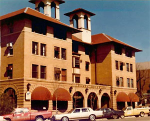 A view of the hotel with large hipped roofs overhanging the building, awnings below and twin towers near the entrance. 