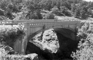 A black and white photo of the bridge with large shadow over the gulch. 