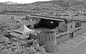 An overhead photo of the fort in black and white with adobe with towers and hills in the background.