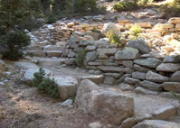 A view of the trail ascending over a series of steps and between a wall of rocks.