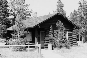 A black and white photo of the station with gabled roof, chimney sticking out in the back and log walls. 