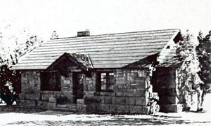 A black and white photo of the house with large stone bricks and gabled roof with low cross gable on the side. 