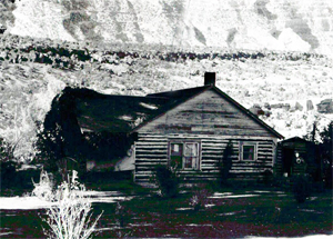 A black and white photo of a building with log walls and gable roof.