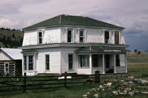 A photo of a house with green hipped roof and two stories of white siding. 