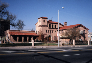 A photo of the building with gabled red roofs and arcade running on the left. 