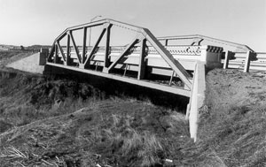 A photo of the bridge in black and white with bowstring arch truss on either side. 