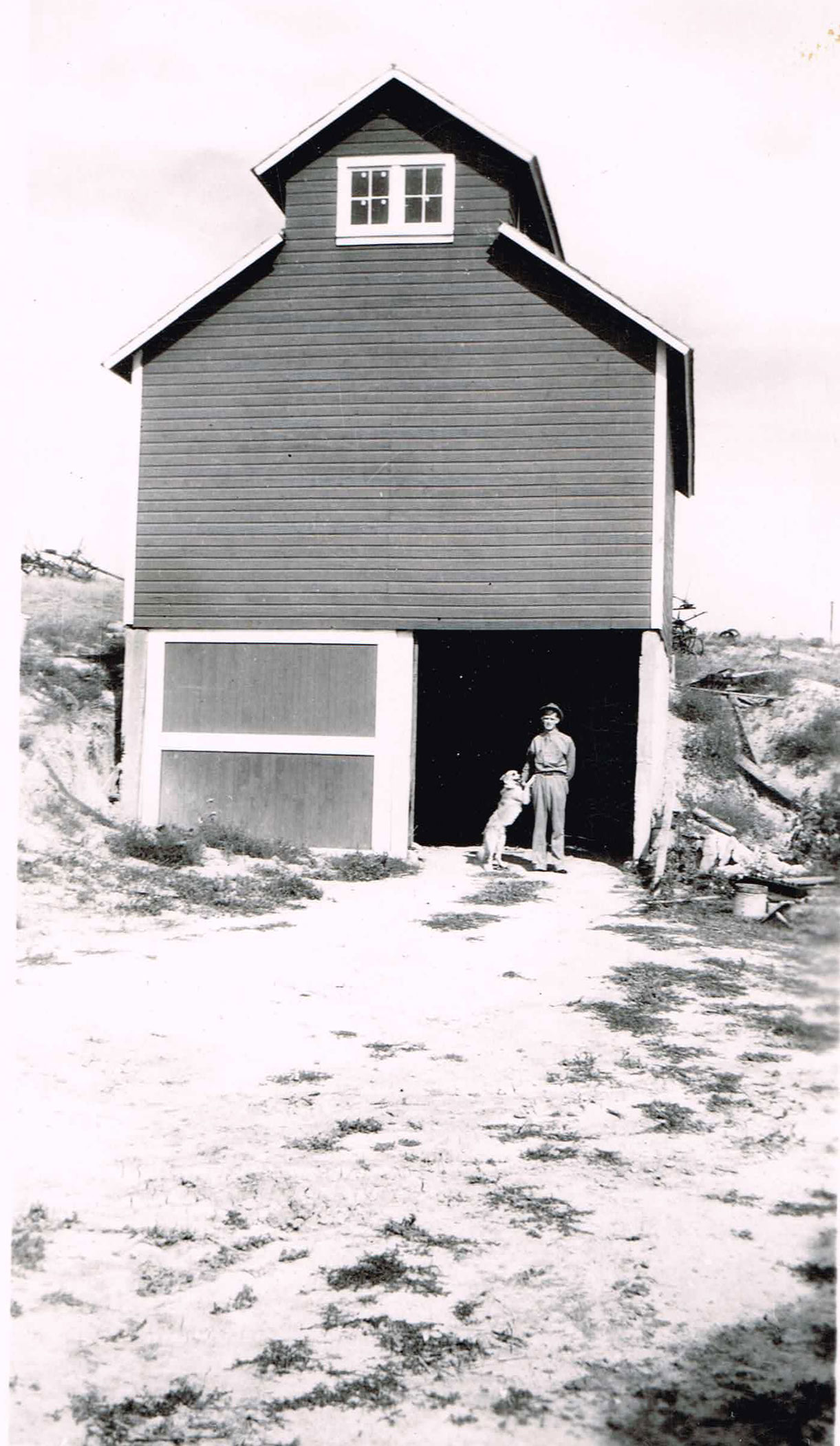 Historic image showing a man and his dog in the doorway of a barn.
