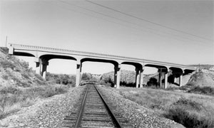 A black and white photo of the viaduct crossing over a set of railroad tracks. 