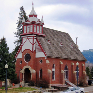 A view of the church from an angle with steep gabled roof, large tower in the center and red walls with pointed windows.
