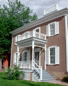 A view of the building with red walls and white trim. There are four windows on top and three and an entrance with raised porch and balcony above.