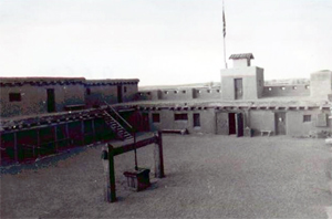 A black and white photo of the fort from the interior with walls on the side, tower on the right and well in the center.