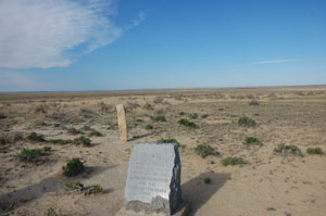 A view of a marker stone before a dusty field. 