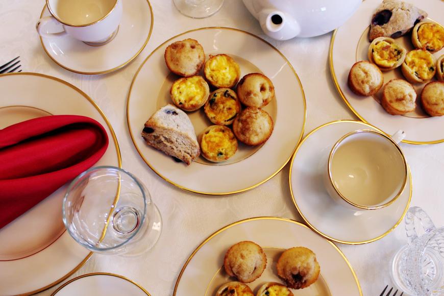 A table setting full of ceramic teacups and plates with a red napkin.  There are scones and quiches displayed on the plates.