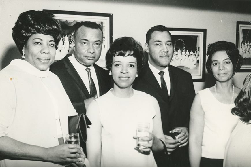 A black and white photo of 5 African American people wearing dresses and suits, holding drinks and looking at the camera. On the photo is written The Owl Club of Denver 1968 Easter C.T. Party.