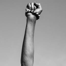 Black and white photo of a raise fist in protest, wearing a beaded bracelet.