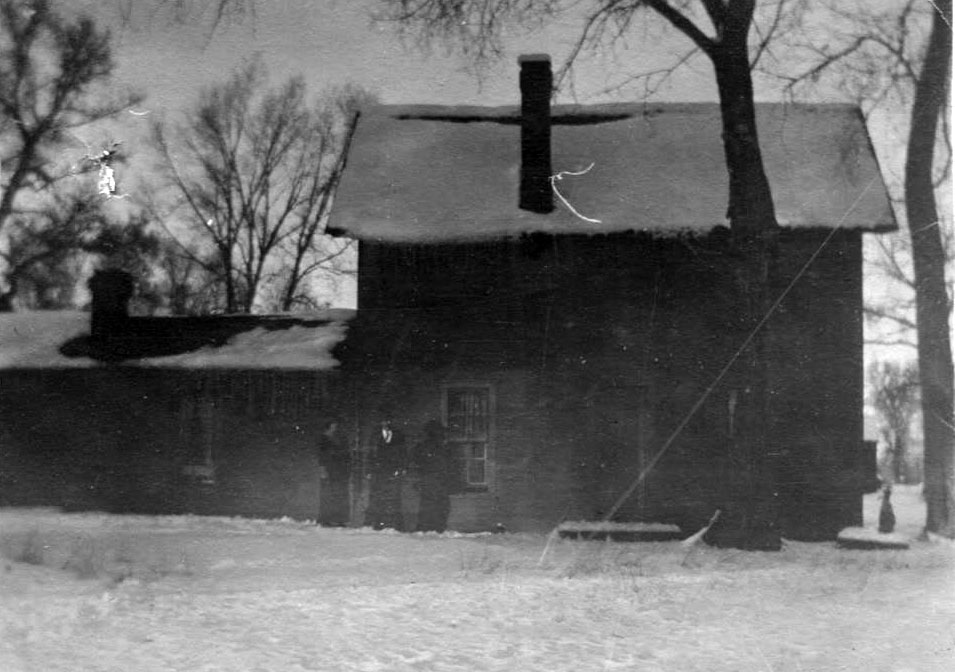 An historic photo showing three people standing outside the Knoblauch Ranch original homestead in the snow, in the early 1900s