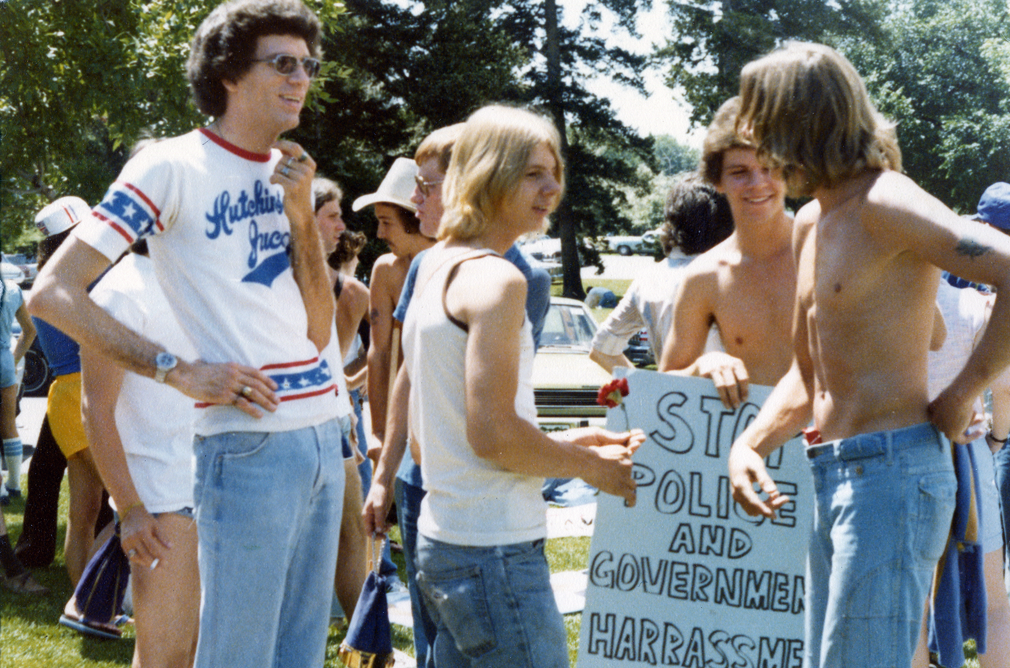 A group of young men, one holding a picket sign, standing in a park.
