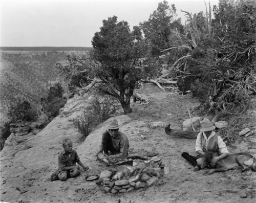 Park Superintendent Jesse Nusbaum (center) tending a campfire at Mesa Verde National Park with Eric O'Brian (left) and wife Aileen Nusbaum (right) with a dog. The photograph was taken by George Lytle Beam, circa 1924.