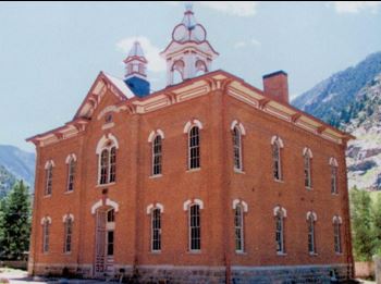 A two-story red brick school house with a gable peak at its entrance. Each window has an arched frame. 