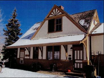 A two-story railroad depot with a gable roof. The roof extends over a small porch at the front of the building. The building is painted white with brown trim. 