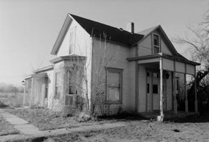 A black and white photo of a building from a corner view with gabled roof and bay window in front.