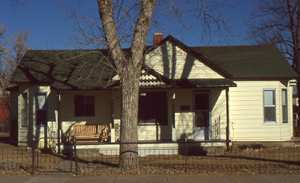 A front view of the house with vovered porch and large tree in the foreground.