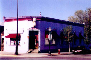 A view of the building with clipped corner containing the entrance, there are a few awnings on either side. 