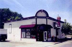A view of the building from a corner. The building has a clipped corner and small awning next to the entrance. 