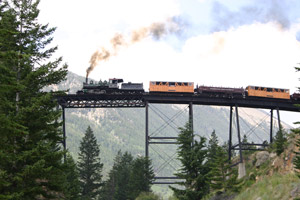 The train passes over a high bridge as smoke emits from its stack