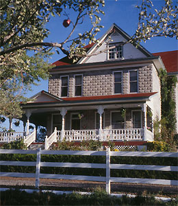 A picture of the house with large covered porch, brick walls and white gable beneath red roof. 