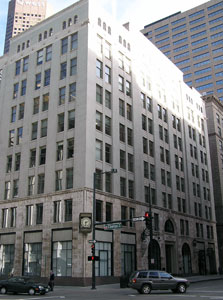 A corner view of the building with rows of tall windows on either side and stoplight and cars on street in front.