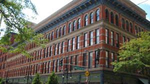 A view of the building  with vibrant red brick stratified by floors and parted by rows of windows, with tree branches sticking out on the sides. 