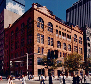 A view of the red building from a slight angle with elaborate arched windows and triangular-capped bookended facade and people on the ground below. 