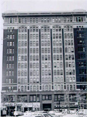 A black and white view of the front of the building, with rows of windows framed by a darker brick. 