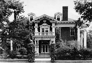A direct view of the mansion in black and white, with large trees on the left and partially on the right. 