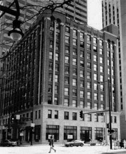 A black and white photo of the building from a slight angle with dark top and lighter bottom. 