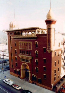 An elevated view of the red building with white-trimmed circular arches and onion-domed minarets on either side and arcade on the top floor. 