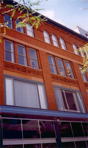 A view looking up at the building at a slight angle shows large lower level windows growing steadily smaller on a background of red brick. 